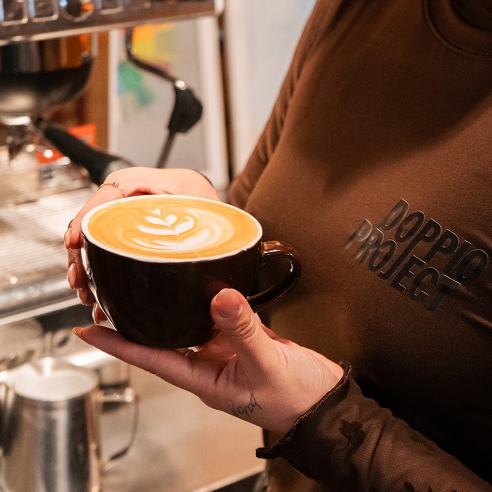 Taza de café con latte art y buzo de Doppio Project